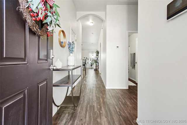 foyer featuring arched walkways, dark wood finished floors, and baseboards