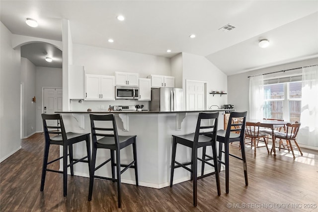 kitchen featuring dark countertops, appliances with stainless steel finishes, a kitchen breakfast bar, arched walkways, and white cabinetry