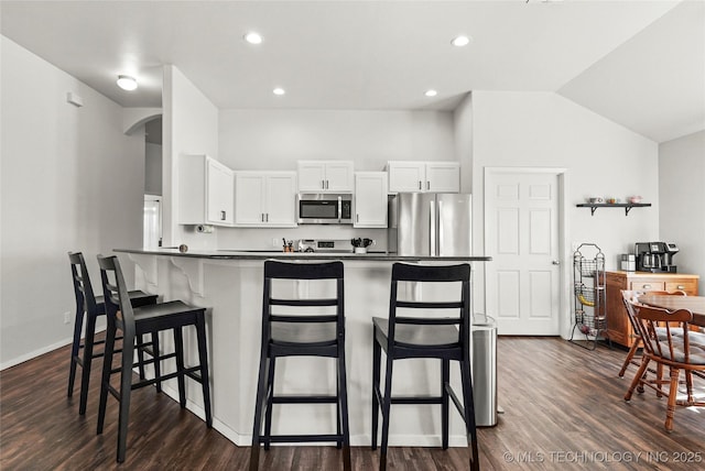 kitchen featuring dark countertops, a kitchen bar, appliances with stainless steel finishes, dark wood-style floors, and white cabinetry