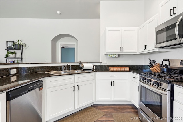 kitchen featuring dark stone counters, arched walkways, a sink, stainless steel appliances, and white cabinets