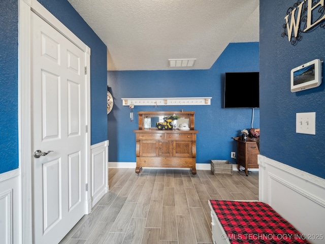 interior space with a textured ceiling, a textured wall, visible vents, baseboards, and wood tiled floor