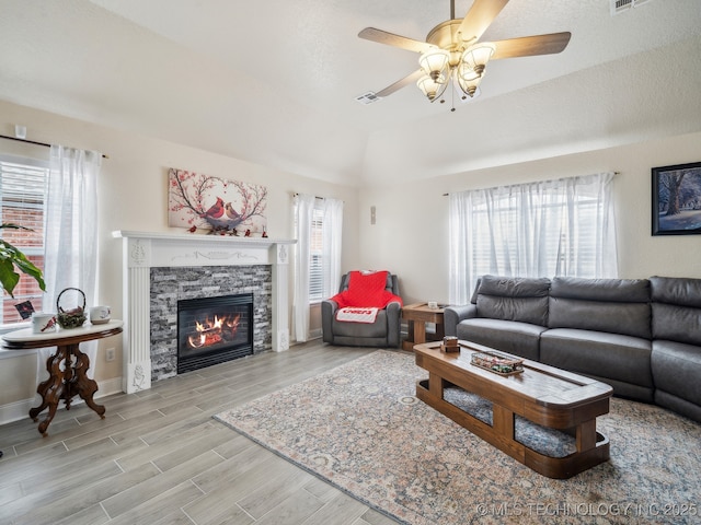 living area with ceiling fan, baseboards, wood finished floors, and a stone fireplace