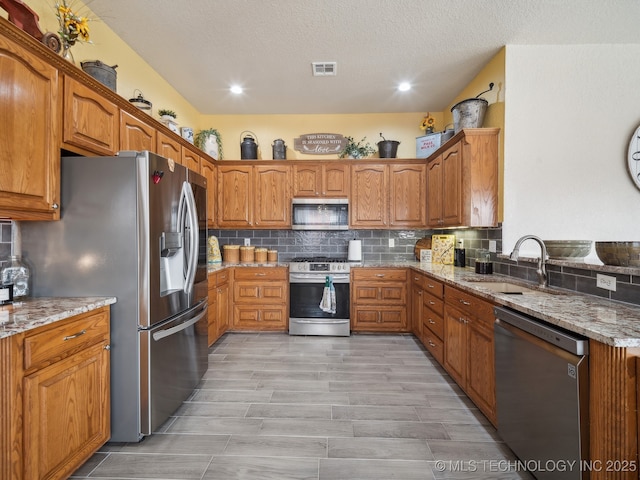 kitchen with light stone counters, appliances with stainless steel finishes, a sink, and visible vents