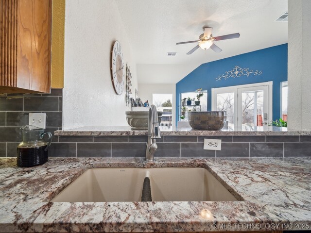 kitchen with stone counters, tasteful backsplash, visible vents, and a sink