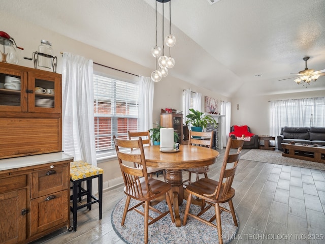 dining area featuring ceiling fan, a textured ceiling, baseboards, vaulted ceiling, and light wood finished floors