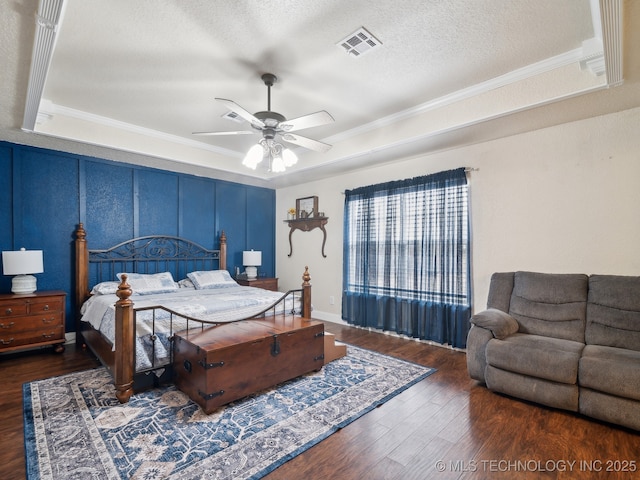 bedroom featuring a textured ceiling, wood finished floors, visible vents, ornamental molding, and a raised ceiling