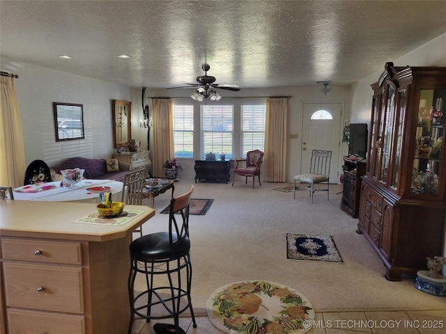 kitchen featuring a textured ceiling, a breakfast bar area, light carpet, a ceiling fan, and light countertops