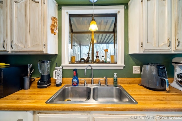 kitchen featuring hanging light fixtures, butcher block counters, white cabinets, and a sink