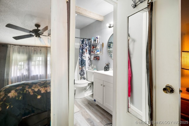 bathroom with ceiling fan, toilet, wood finished floors, vanity, and beamed ceiling