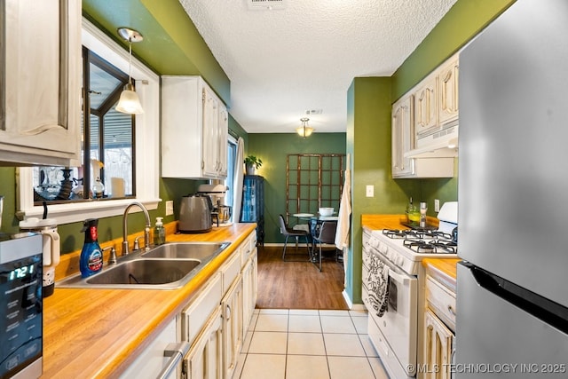 kitchen with light tile patterned floors, a textured ceiling, stainless steel appliances, a sink, and pendant lighting