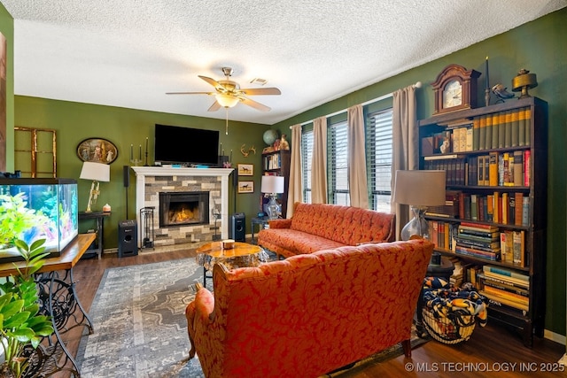 living area featuring a textured ceiling, a fireplace, wood finished floors, a ceiling fan, and baseboards