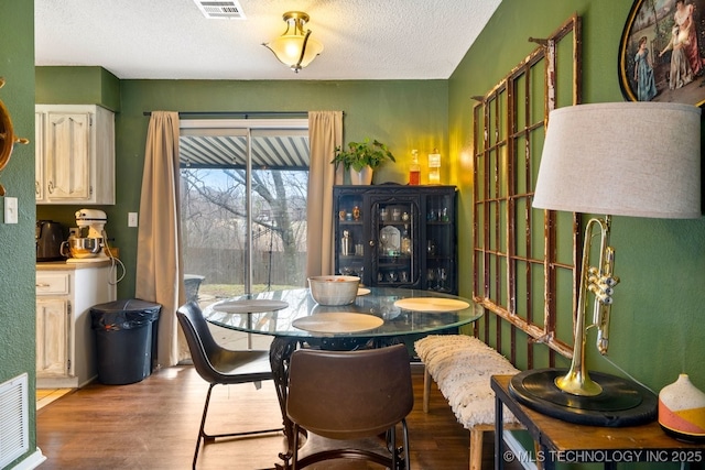 dining area with a textured ceiling, wood finished floors, and visible vents