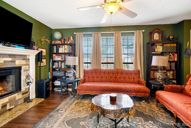 living area with ceiling fan, a fireplace, a textured ceiling, and wood finished floors