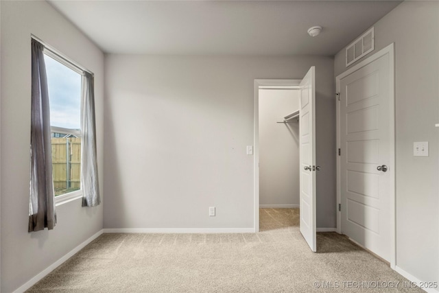 unfurnished bedroom with baseboards, visible vents, a walk in closet, and light colored carpet