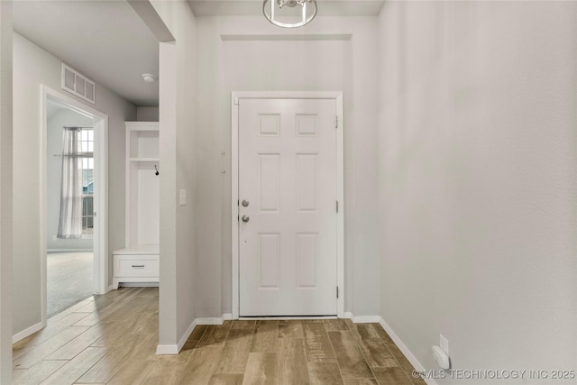 doorway to outside with baseboards, visible vents, and light wood finished floors