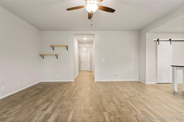 unfurnished living room featuring light wood-style floors, ceiling fan, baseboards, and a barn door