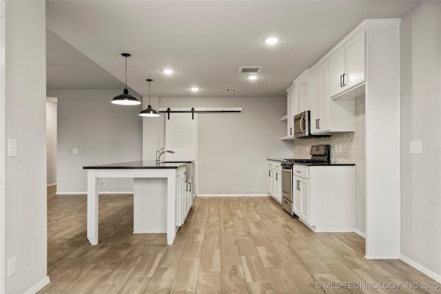 kitchen with a barn door, white cabinets, appliances with stainless steel finishes, tasteful backsplash, and dark countertops