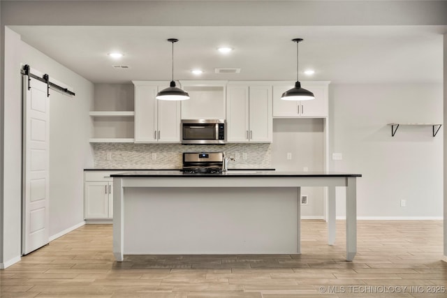 kitchen with a barn door, stainless steel appliances, white cabinets, open shelves, and dark countertops