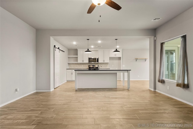 kitchen featuring a barn door, stainless steel appliances, visible vents, open shelves, and dark countertops