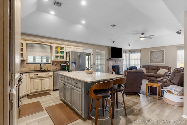 kitchen with a sink, visible vents, a kitchen breakfast bar, a lit fireplace, and appliances with stainless steel finishes