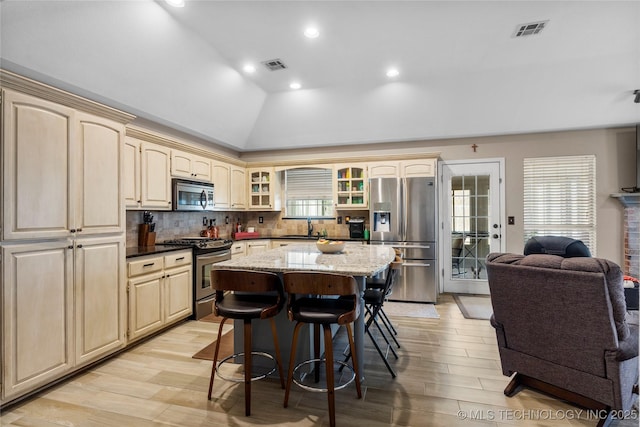 kitchen featuring appliances with stainless steel finishes, glass insert cabinets, visible vents, and a kitchen breakfast bar