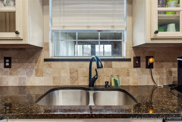 kitchen featuring cream cabinets, dark stone counters, backsplash, and a sink