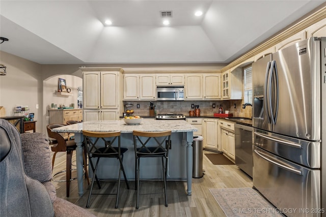 kitchen with arched walkways, stainless steel appliances, lofted ceiling, visible vents, and a kitchen bar