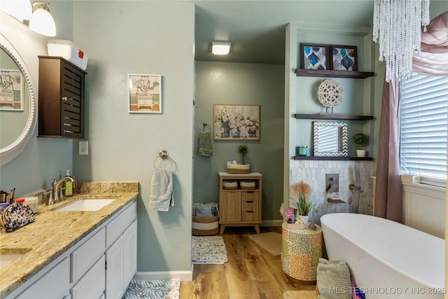 full bath with double vanity, baseboards, wood finished floors, a freestanding bath, and a sink