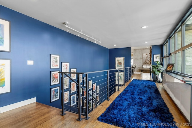 corridor with floor to ceiling windows, wood finished floors, track lighting, an upstairs landing, and baseboards