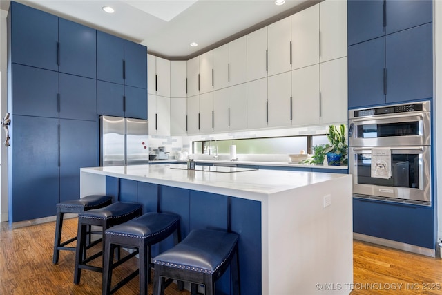 kitchen featuring blue cabinets, light wood-style floors, stainless steel appliances, and a kitchen breakfast bar