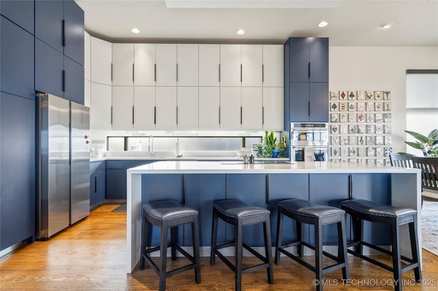 kitchen with appliances with stainless steel finishes, a breakfast bar area, light countertops, light wood-type flooring, and blue cabinetry