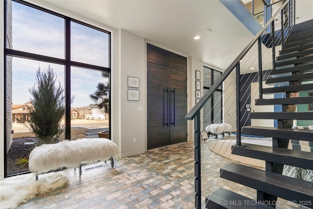 entryway with brick floor, recessed lighting, floor to ceiling windows, and stairs