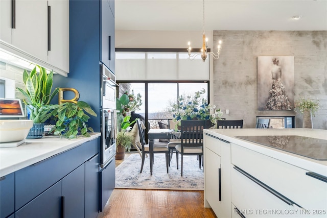 kitchen with dark wood finished floors, blue cabinetry, light countertops, an inviting chandelier, and stainless steel oven