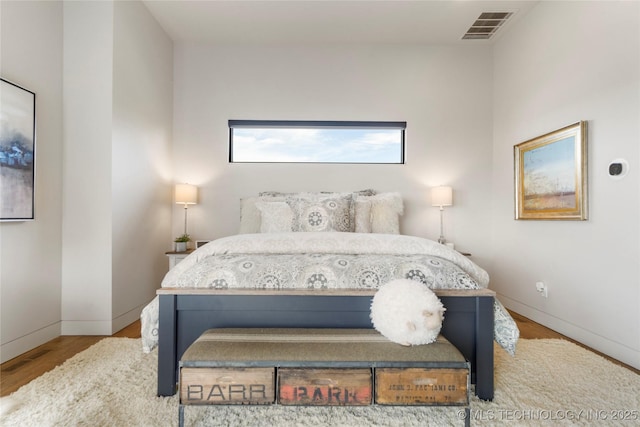 bedroom with baseboards, visible vents, and wood finished floors