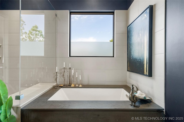 bathroom with a garden tub and tile walls