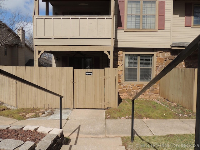 entrance to property with stone siding, fence, and a balcony