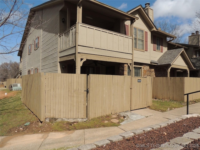 view of property exterior featuring a fenced front yard, a balcony, stone siding, a gate, and a chimney