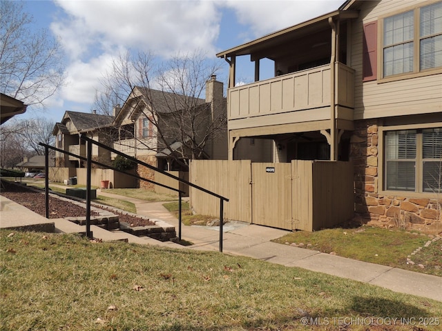 view of side of property featuring stone siding, fence, a balcony, and a gate