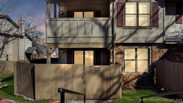 exterior space featuring a balcony, a gate, stone siding, and a fenced front yard