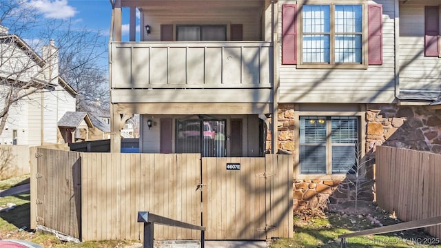 back of property featuring a balcony, a gate, stone siding, and a fenced front yard