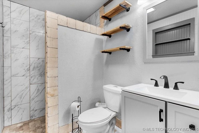 full bath featuring a textured wall, a tile shower, vanity, and toilet