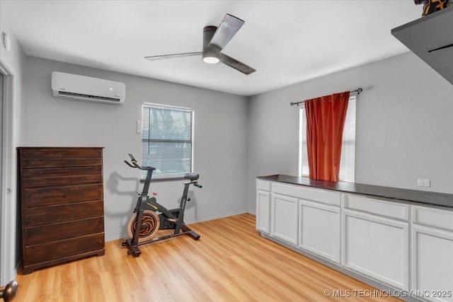 exercise room with a ceiling fan, baseboards, a wall unit AC, and light wood finished floors