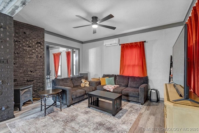 living room featuring ceiling fan, wood finished floors, a wood stove, a textured ceiling, and an AC wall unit