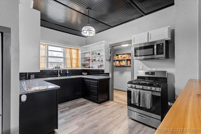 kitchen featuring appliances with stainless steel finishes, hanging light fixtures, light stone countertops, light wood-style floors, and open shelves