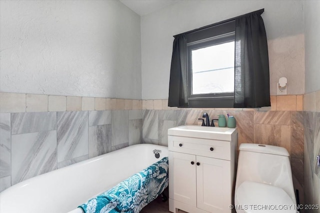 bathroom with a freestanding bath, vanity, toilet, and tile walls