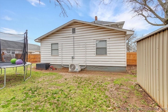 rear view of house featuring ac unit, a trampoline, fence, and a lawn