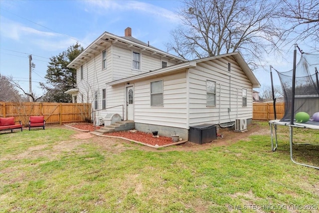 rear view of property with a fenced backyard, a trampoline, a chimney, and a yard