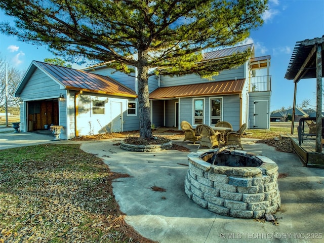 view of front facade featuring an outbuilding, metal roof, a fire pit, concrete driveway, and a patio area