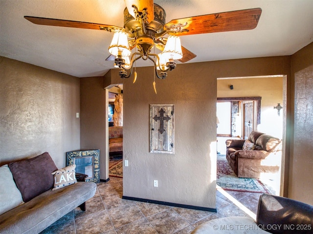 sitting room with arched walkways, a textured wall, a ceiling fan, baseboards, and tile patterned floors