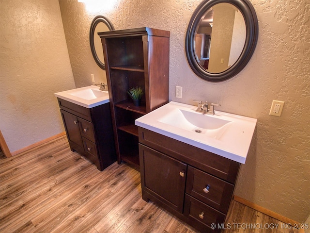 bathroom featuring a textured wall, two vanities, a sink, and wood finished floors